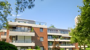 En byggnad med flera våningar, balkonger, en välskött gräsmatta och omgivande grönska.