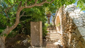 A stone-walled outdoor area with a tiled shower, steps leading to a door, and lush greenery. - Brisa (Son Servera)