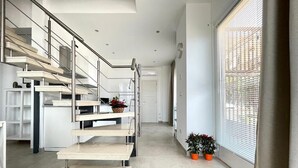 Un intérieur moderne avec un escalier, un coin cuisine et une grande fenêtre équipée de stores.