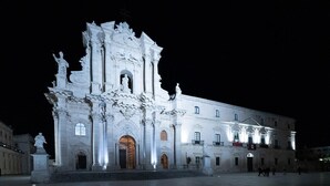 Un imposant bâtiment illuminé, doté d’une architecture riche et ornée, avec une porte d’entrée centrale et de nombreuses statues.