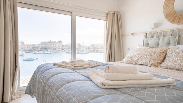 Une chambre avec un grand lit, donnant sur un port de plaisance et offrant une vue sur la ville.