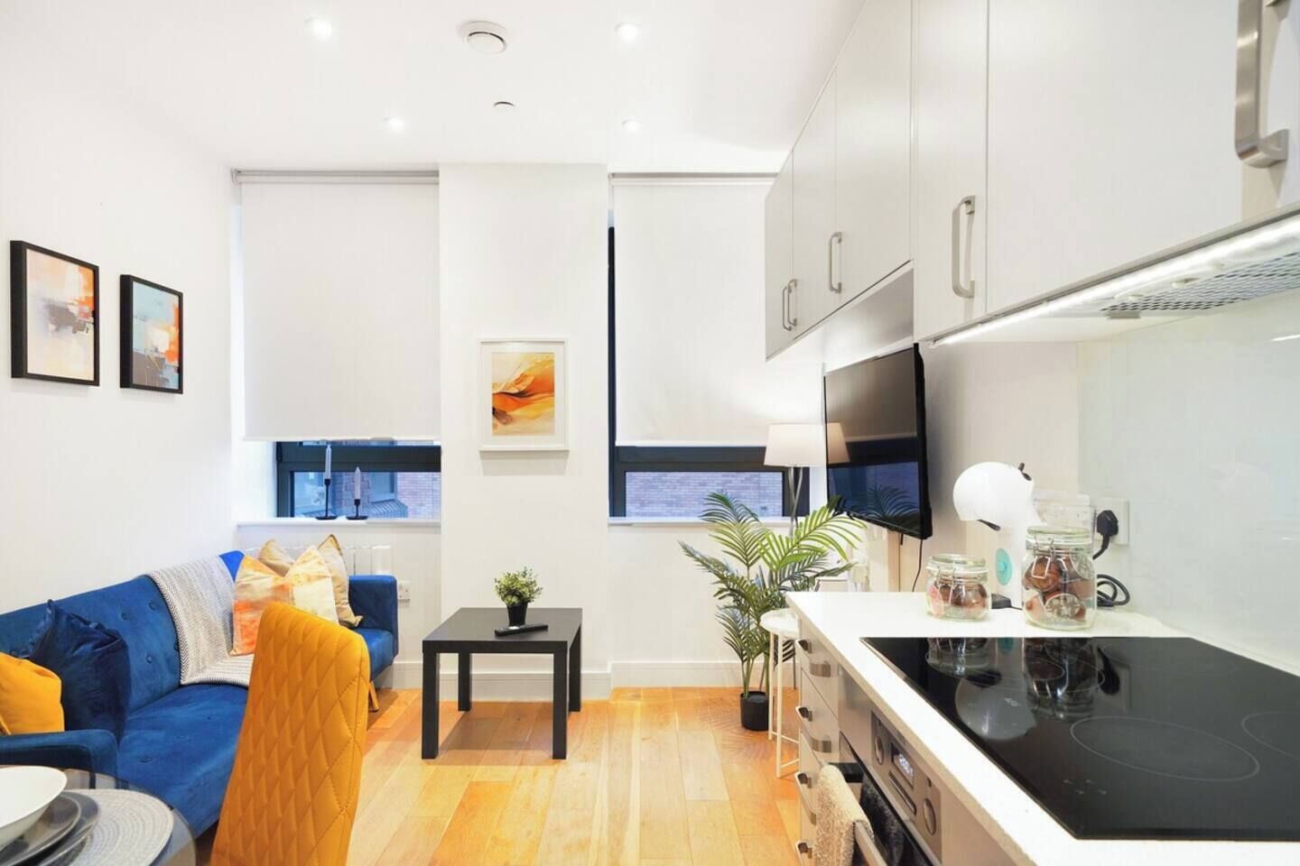 Un salon moderne comprenant un canapé, une petite table et un coin cuisine avec une cuisinière et des placards.