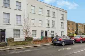 A row of white terraced houses with a brick wall and a small tree in front. - Stylish Kentish Town Home/Private Garden & Jacuzzi (London)