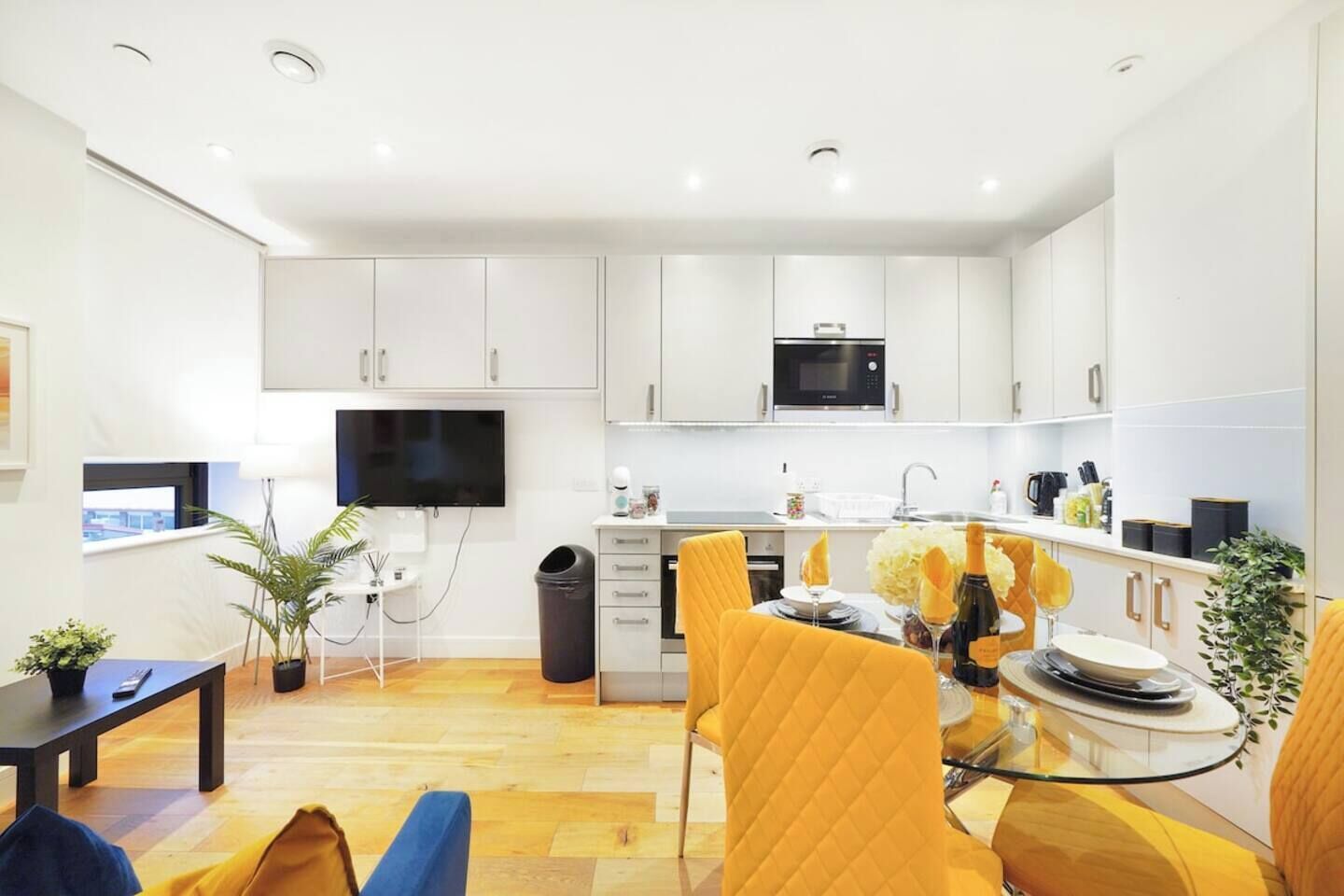 A modern kitchen with white cabinets, a microwave, and a dining area with yellow chairs.