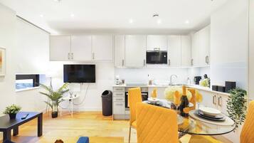 A modern kitchen with white cabinets, a microwave, and a dining area with yellow chairs.