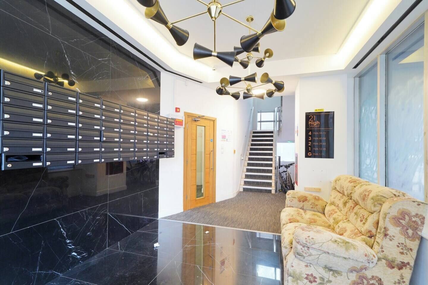 A lobby with a black marble floor, a floral sofa, a staircase, and a wall-mounted mailbox.