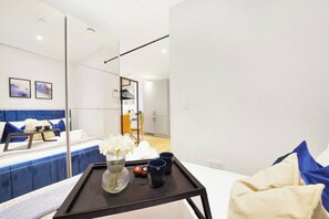A modern hotel room with a bed, bedside table, and a large mirror. - Stylish Feltham Studio near Station & Shops 41 (London)