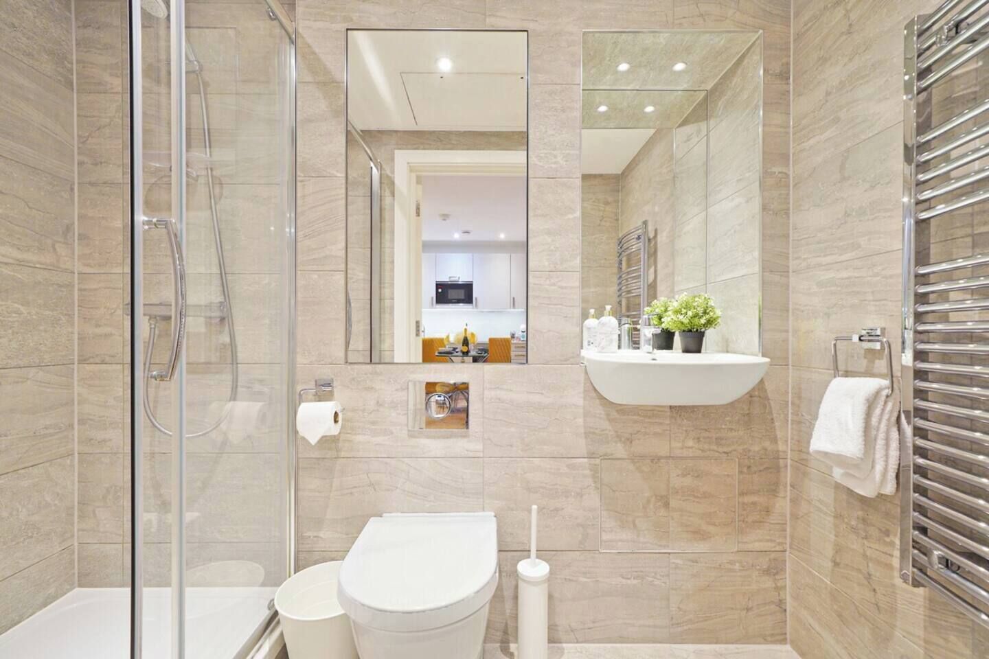 A modern bathroom with a glass shower enclosure, a toilet, a sink with a mirror, and a towel rack.