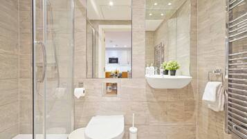 A modern bathroom with a glass shower enclosure, a toilet, a sink with a mirror, and a towel rack.