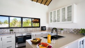 A modern kitchen with white cabinetry, a large window, and a built-in oven. - Villa Greentree Nusa Dua (Kutuh)