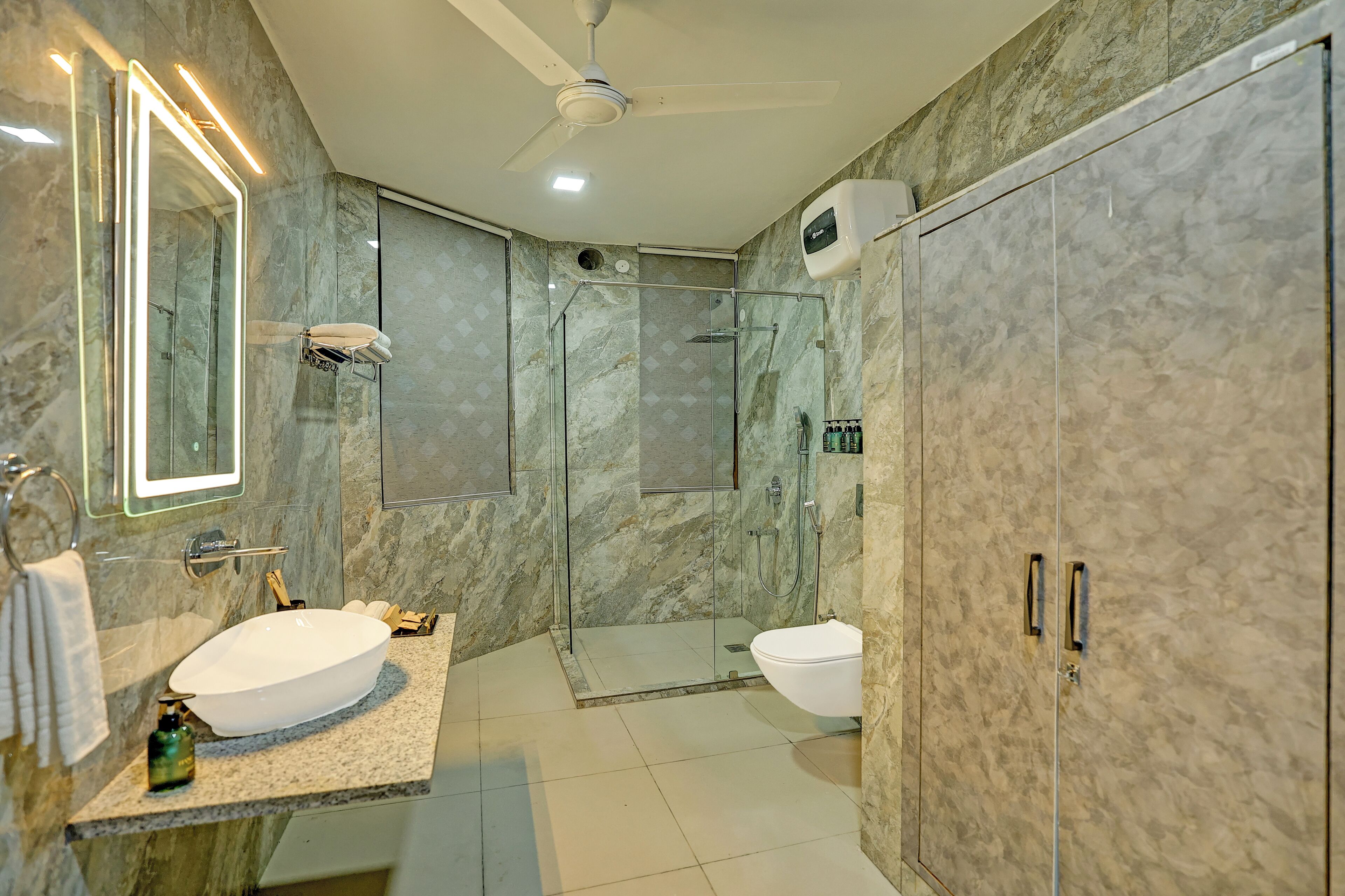 Ein modernes Badezimmer mit einer begehbaren Glasdusche, einem weißen Waschbecken und Marmorwänden.