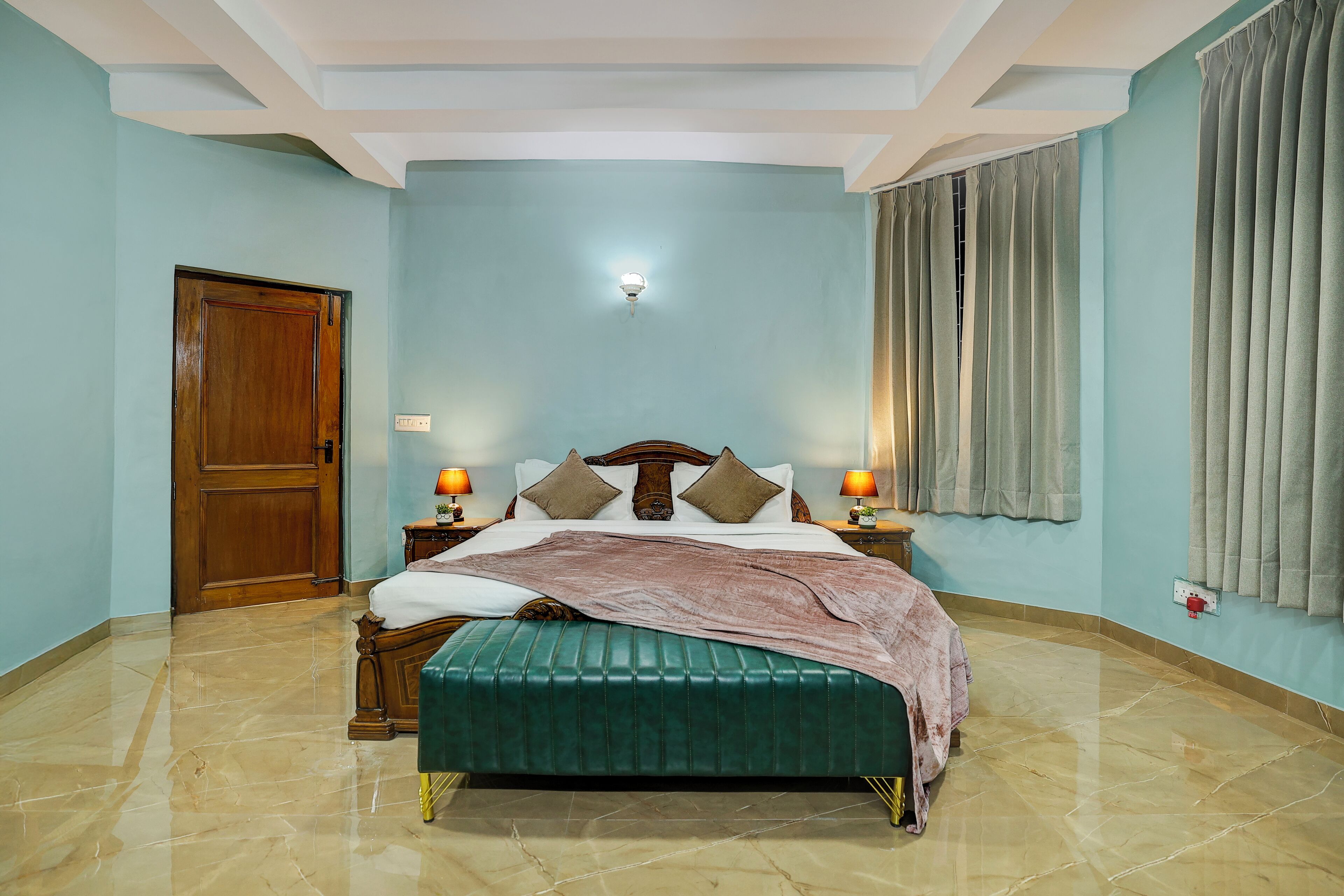 Un dormitorio con una cama de madera, un banco tapizado en verde, paredes azul claro y una puerta de madera.