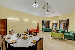 A dining area with a round table set for four, surrounded by green sofas and a green armchair. - Alaya Stays Casa Avakasha 4 BHK Villa  (Gurugram)