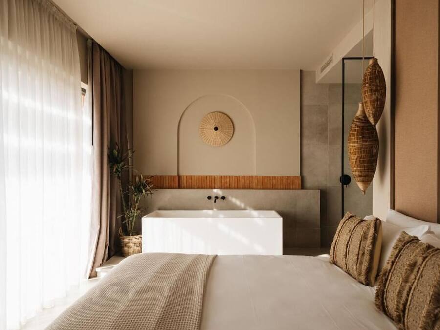 Una habitación de hotel moderna con una cama grande, una bañera integrada y un ventanal con cortinas.