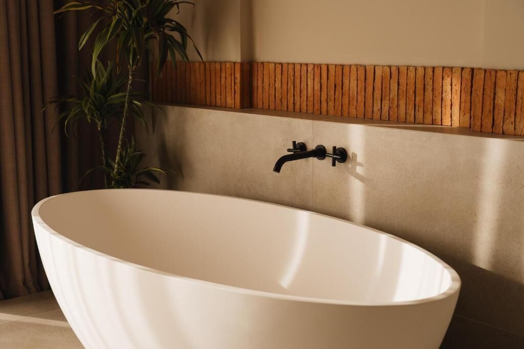 A freestanding bathtub in a bathroom with a wooden panel design on the wall behind it.