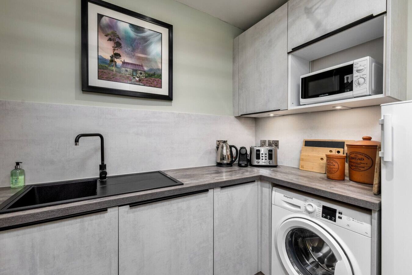 A compact kitchen with a built-in washing machine, a microwave, and a coffee maker.