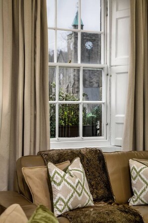 Ein Zimmer mit großem Fenster, einem braunen Sofa und Blick auf ein Gebäude mit einem Uhrturm.