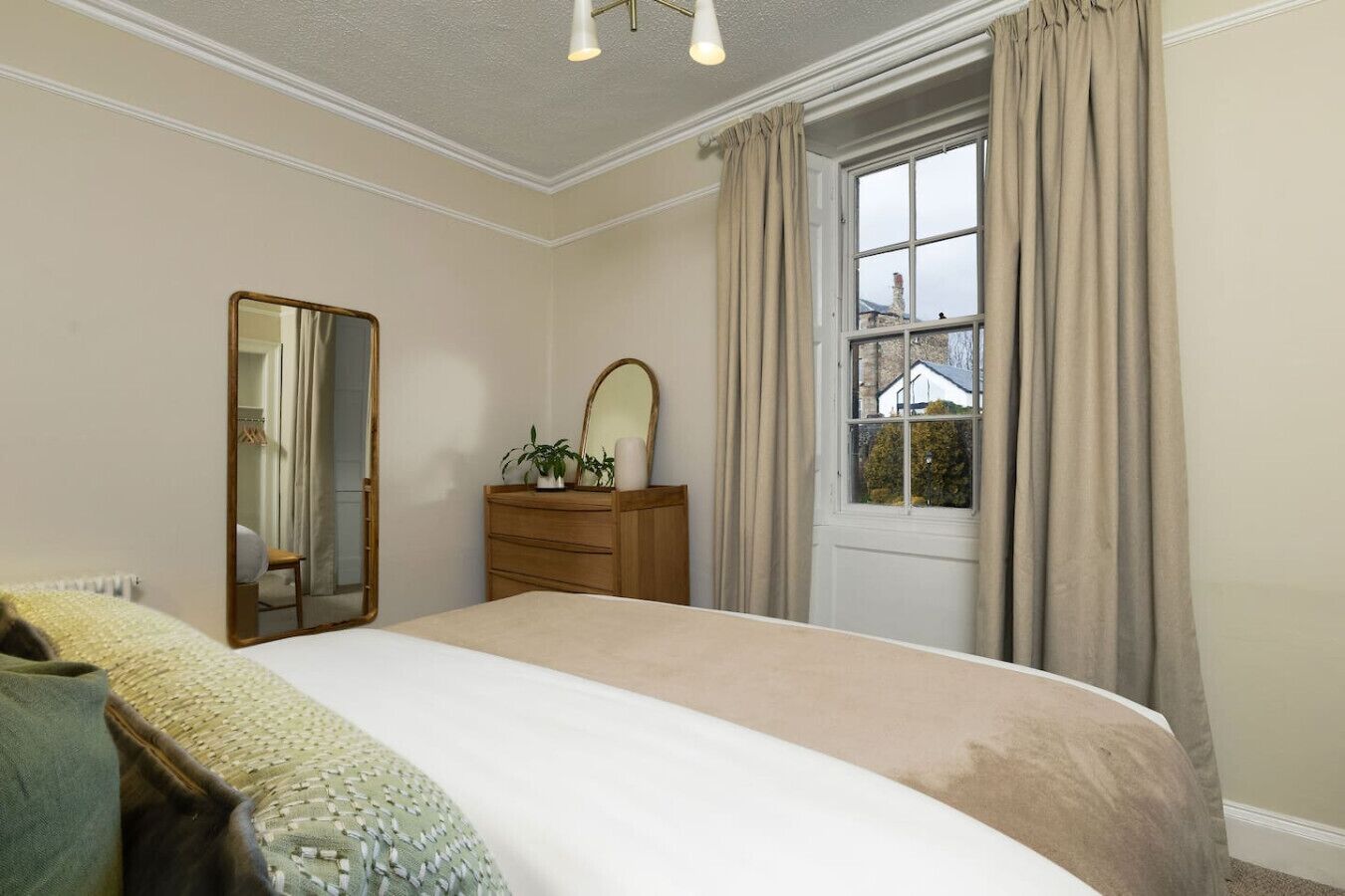 Une chambre à coucher avec un lit, une commode, un miroir et une fenêtre avec des rideaux.