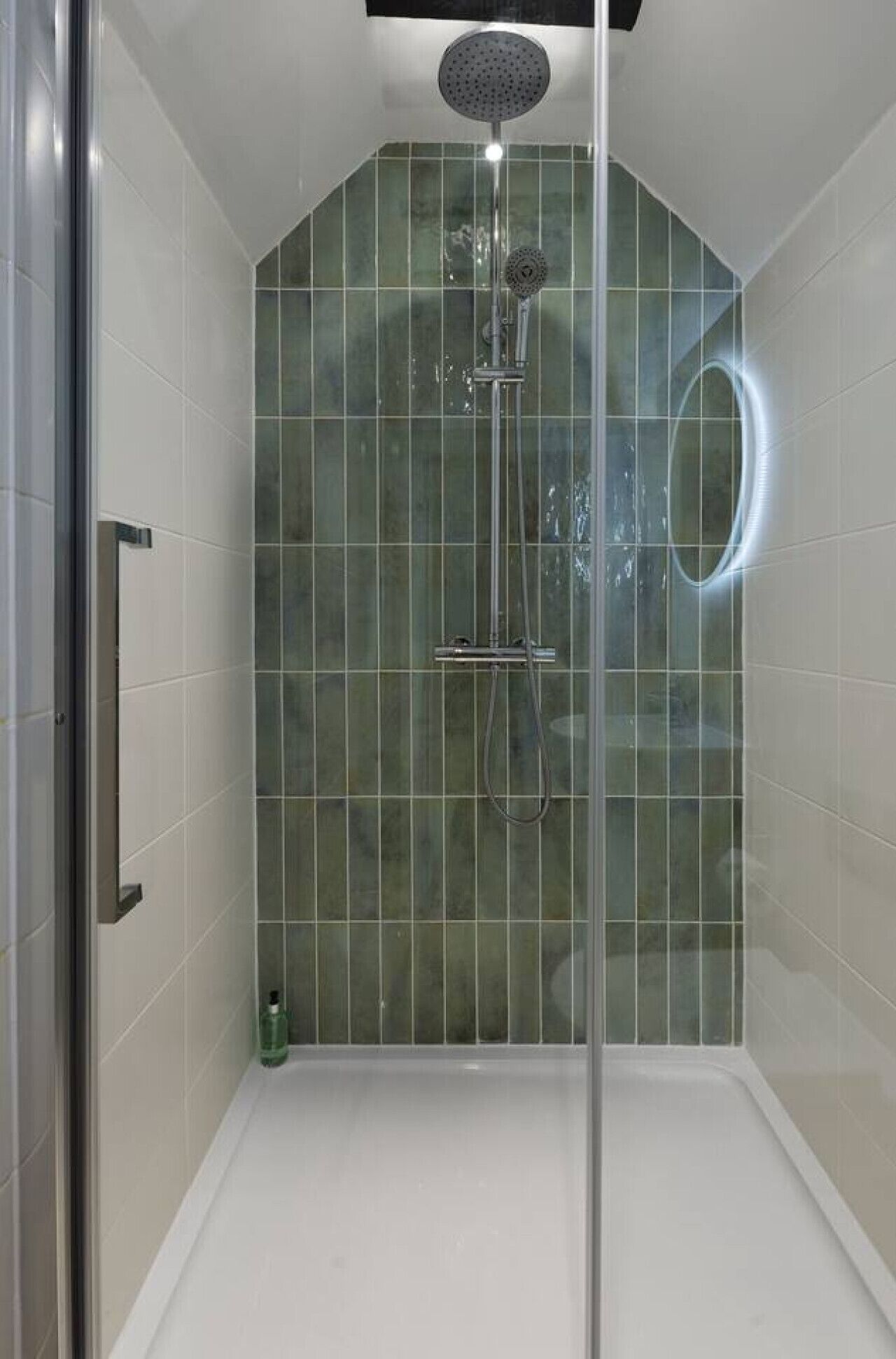 Une douche moderne avec une porte en verre, des murs recouverts de carreaux verts et une pomme de douche à main.
