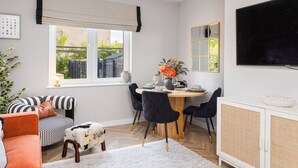 A modern living room with a dining area, a sofa, a TV, and a window with a view of the outside. - Paradykes House - Free Parking & Garden (Midlothian)