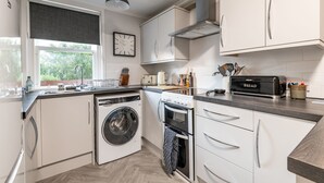 Una cucina moderna con mobili bianchi, lavatrice integrata, forno e tostapane.