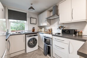Eine moderne Küche mit weißen Schränken, einer eingebauten Waschmaschine, einem Backofen und einem Toaster.