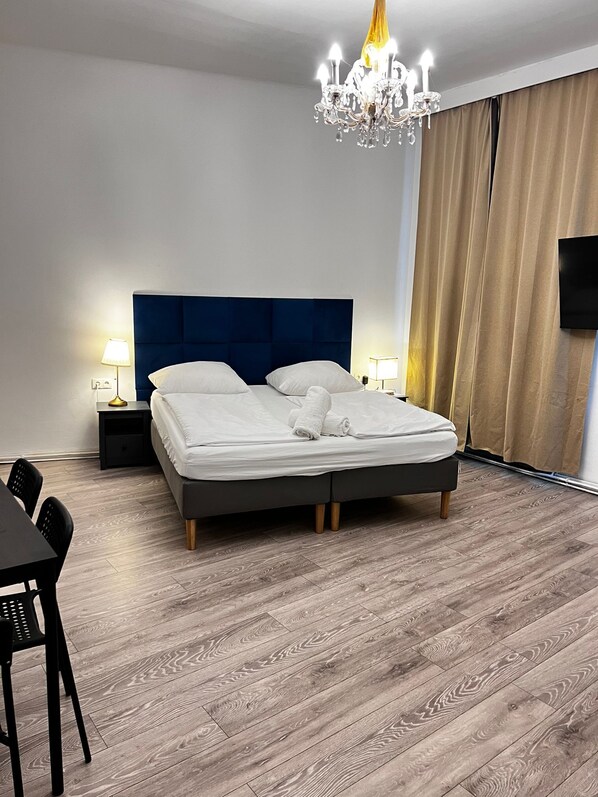 Moderni hotellihuone, jossa on suuri sänky, kattokruunu, taulutelevisio ja ruokailutila.