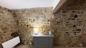 A room with a stone wall, a wooden floor, a grey dresser, and a white lamp. - Apartment in the historic center of Honfleur (Honfleur)