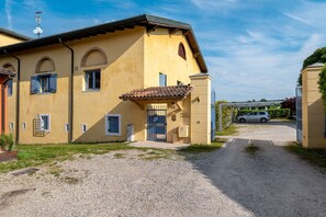 Eine gelbe Villa mit Kiesweg, geschlossenem Eingangstor und einem geparkten Auto im Hintergrund.