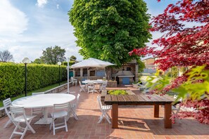 Eine Terrasse mit rundem Tisch und Stühlen, einer Holzbank und einem Grill.