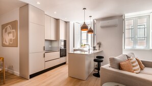 Eine moderne Küche mit einer zentralen Kochinsel, Pendelleuchten und einem Essbereich mit einer Couch und einem Couchtisch.