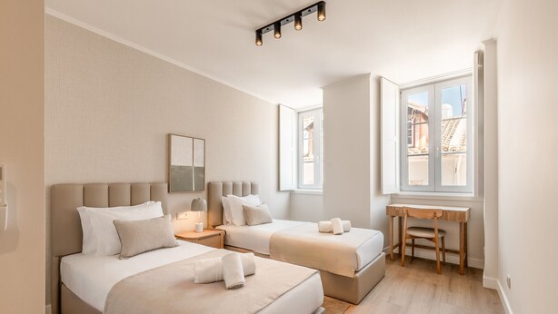 Ein Hotelzimmer mit zwei Betten, einem Schreibtisch und einem Fenster mit Blick auf Gebäude.