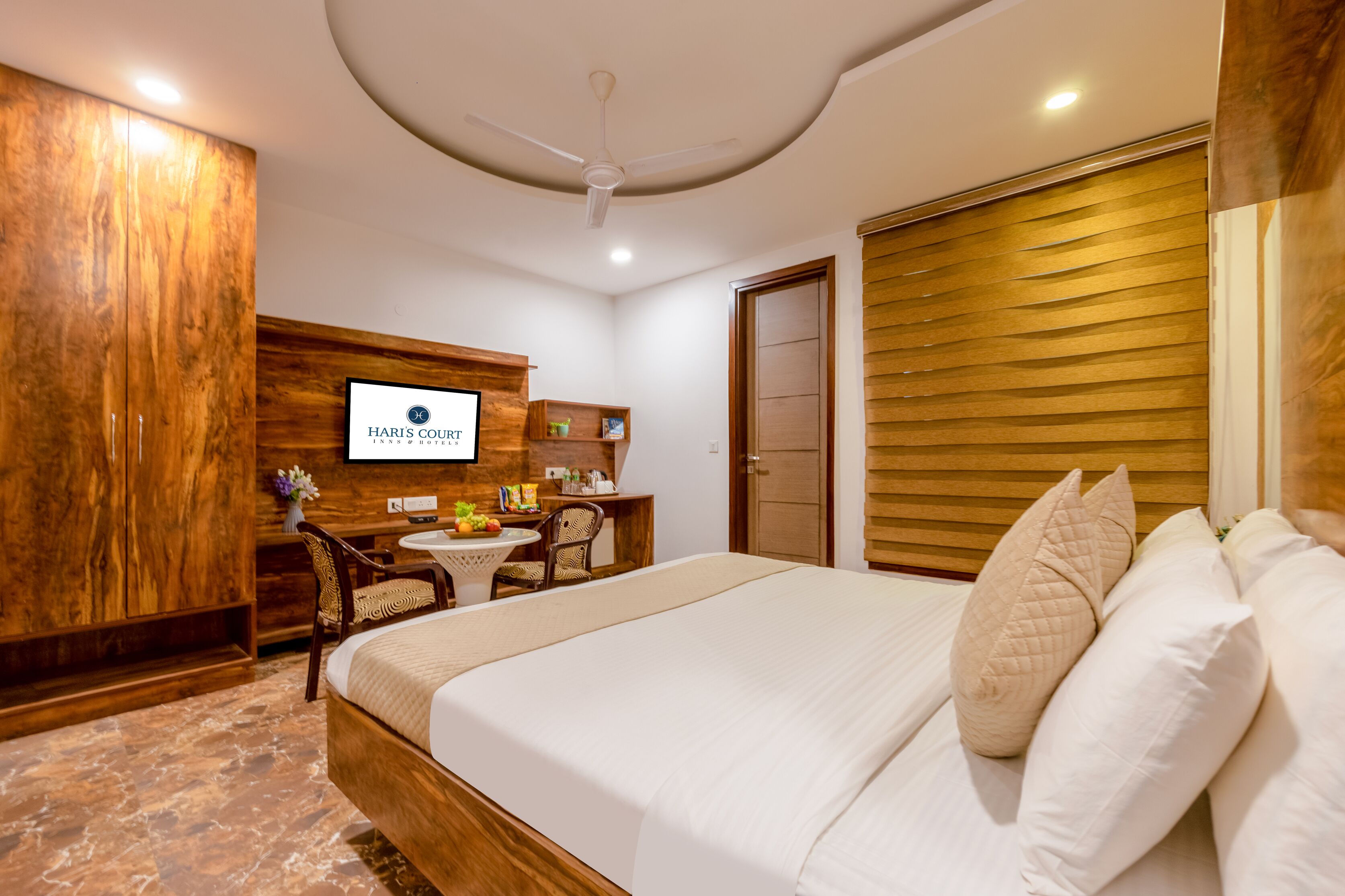 A hotel room with a bed, a desk with a chair, a television, and a wooden wardrobe.