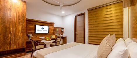 A hotel room with a bed, a desk with a chair, a television, and a wooden wardrobe.