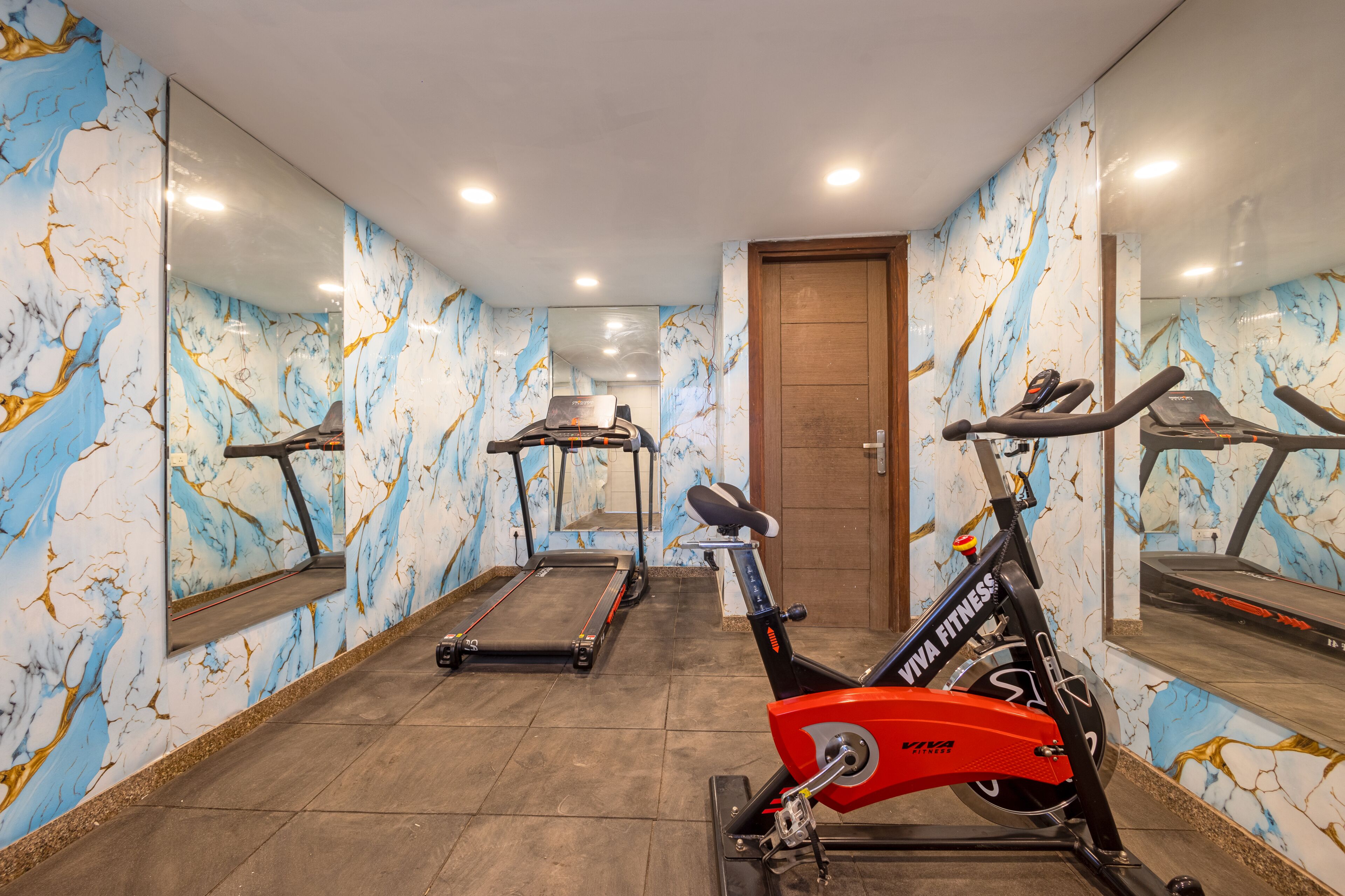 A gym with exercise equipment, marble-patterned walls, and a wooden door.