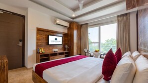 Ein Hotelzimmer mit Bett, Wandfernseher, Schreibtisch mit Stuhl und einem Fenster mit Vorhängen.
