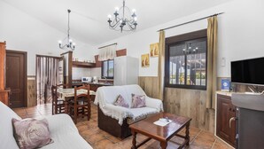 Una sala de estar con un sofá, una mesa de centro, una zona de comedor con una mesa y sillas, una cocina con un refrigerador y un televisor.