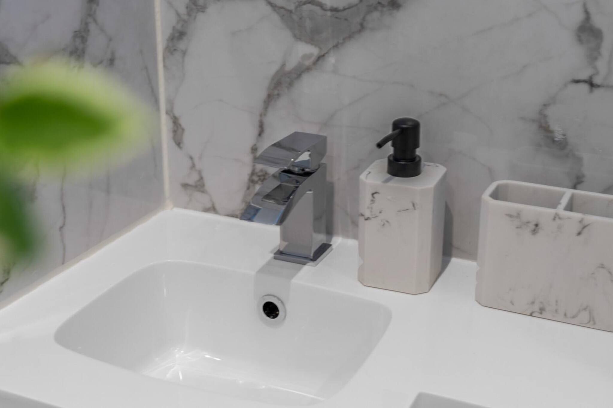 A bathroom sink with a modern faucet, a soap dispenser, and a marble-patterned wall.