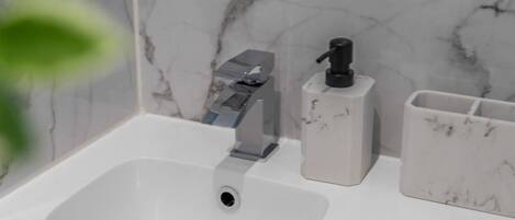 A bathroom sink with a modern faucet, a soap dispenser, and a marble-patterned wall.