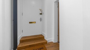Un couloir intérieur propre et aux murs blancs, avec un escalier en bois menant à une porte dotée d’une poignée en laiton et d’une petite plaque en laiton.