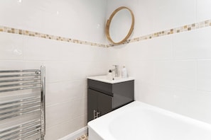 Une salle de bain avec des carreaux blancs, un miroir rond, un lavabo avec des articles de toilette et une baignoire.