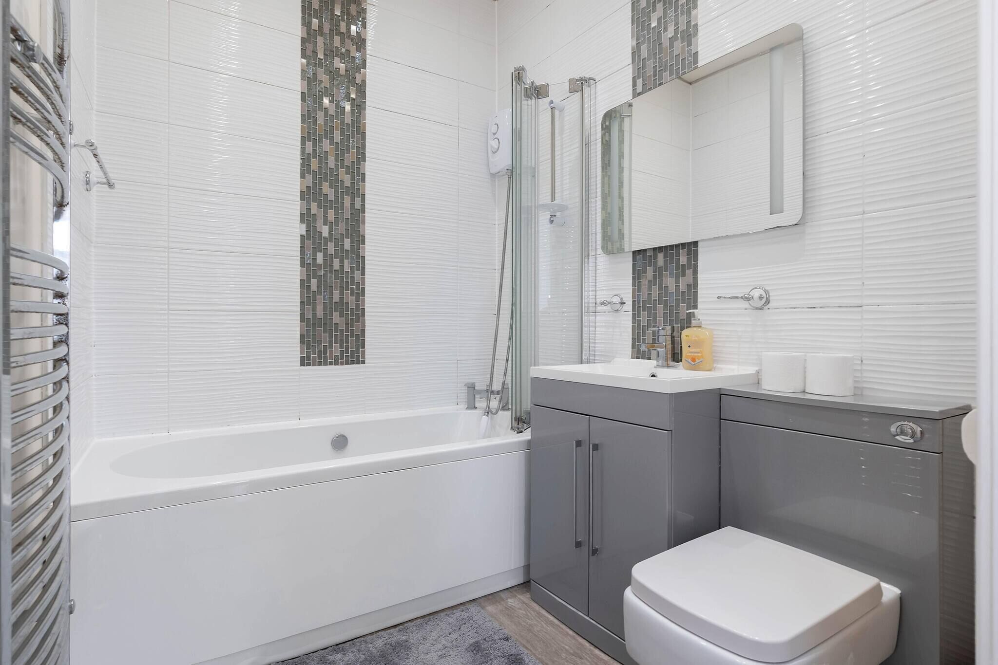 A modern bathroom with a white bathtub, grey cabinets, and a white toilet.