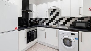 Une cuisine compacte avec des meubles blancs, un pare-feu noir et blanc, un four à micro-ondes encastré, un lave-vaisselle et une machine à laver.