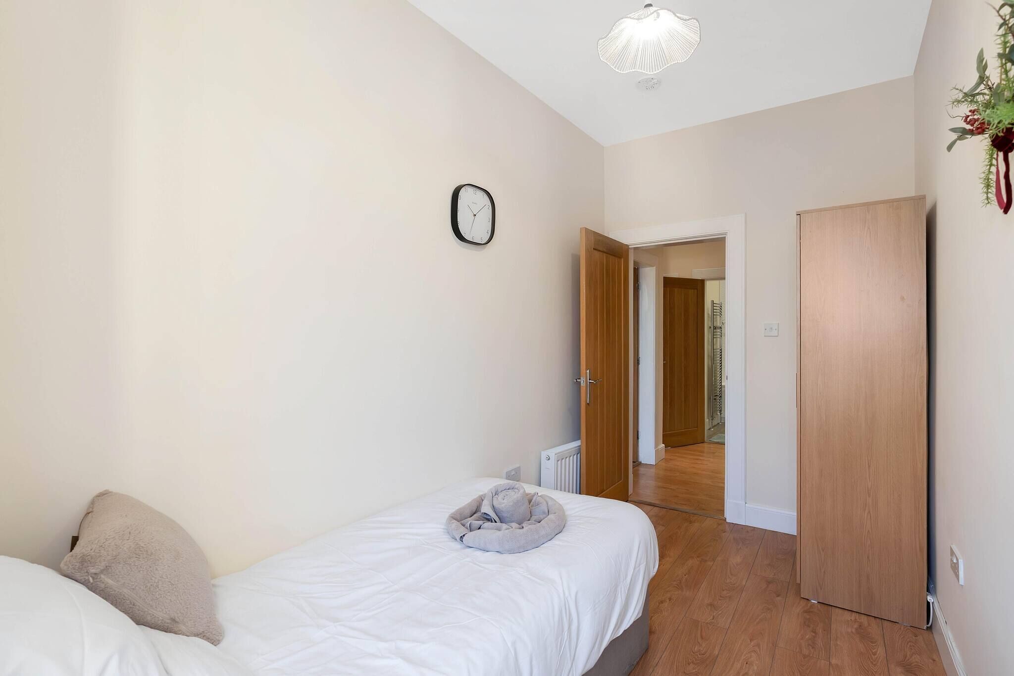 A bedroom with a bed, a bedside table, a clock, a radiator, and a wooden wardrobe.