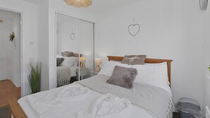 Una cama bien hecha con cabecera de madera, una lámpara de noche y una decoración con forma de corazón en la pared.