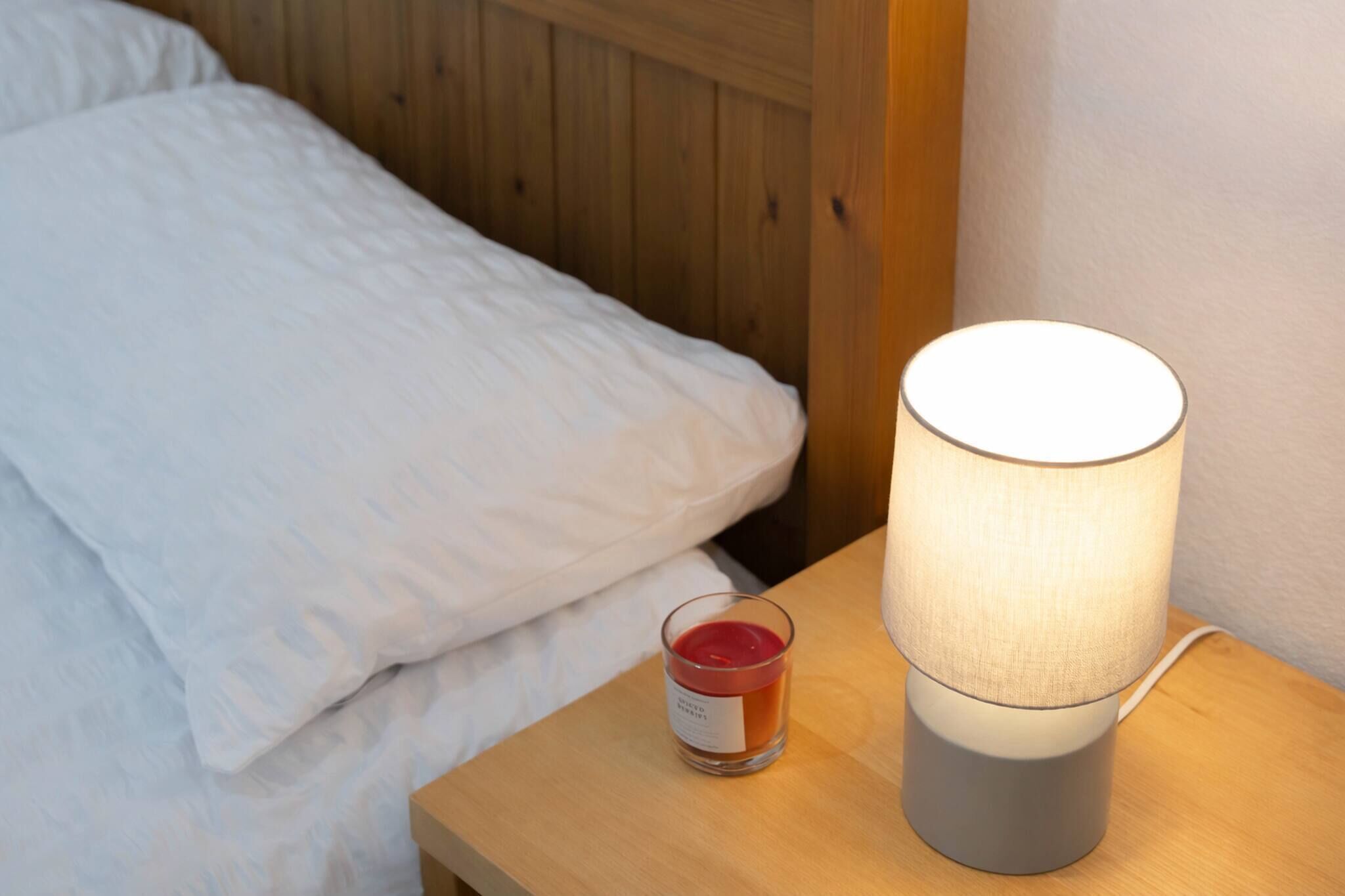 A wooden bedside table with a white lamp and a glass candle.