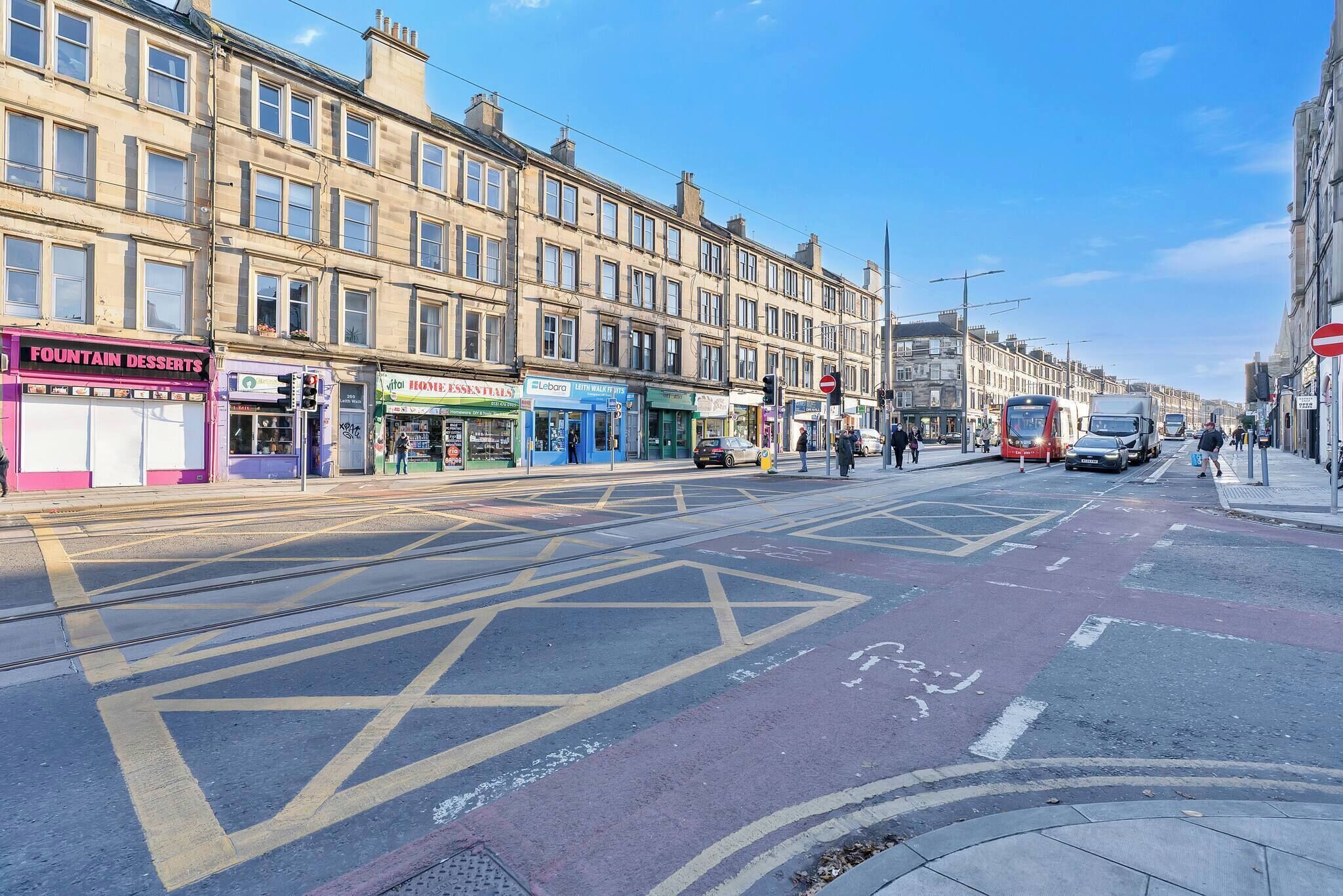 A street with shops, including a bakery and a dessert shop, and tram tracks.
