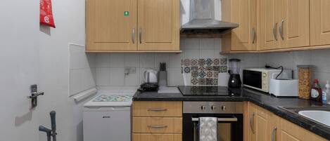 A compact kitchen with wooden cabinets, a microwave, a toaster, and a kettle.