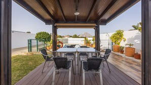 Een terras buiten met een houten terras, een tafel met stoelen en potplanten.
