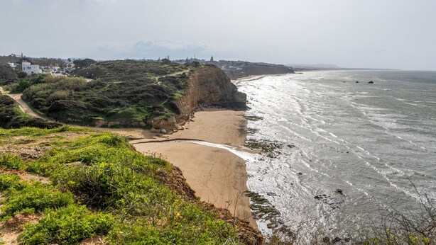 Een kustlandschap met een zandstrand, rotsachtige kliffen en uitzicht op de oceaan.